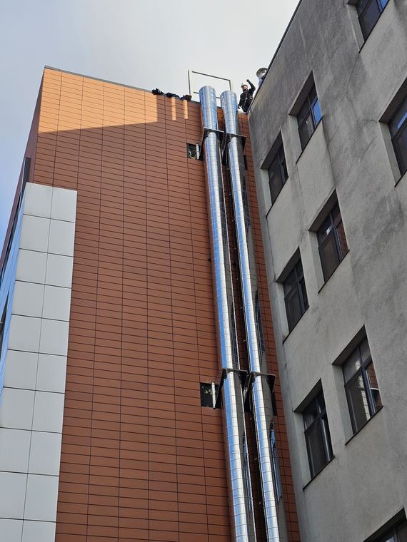 Două coșuri de fum din inox montate pe fațada unei clădiri, între corpuri de clădire